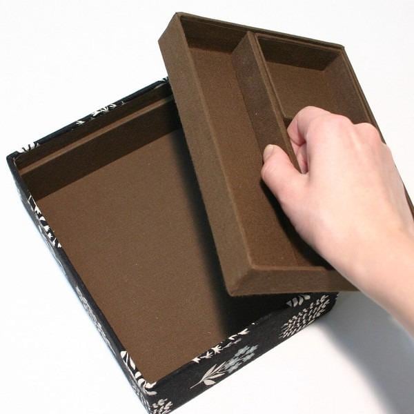 A hand is opening a brown box with a floral pattern on the lid.