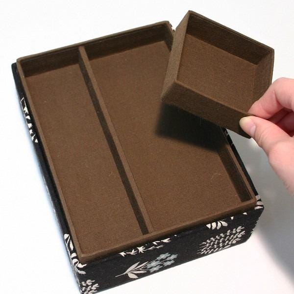 A hand is holding a brown box with a floral pattern, and the box appears to be empty.