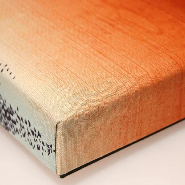 a close-up view of a textured surface, possibly a piece of fabric or paper, with a warm orange and beige gradient.