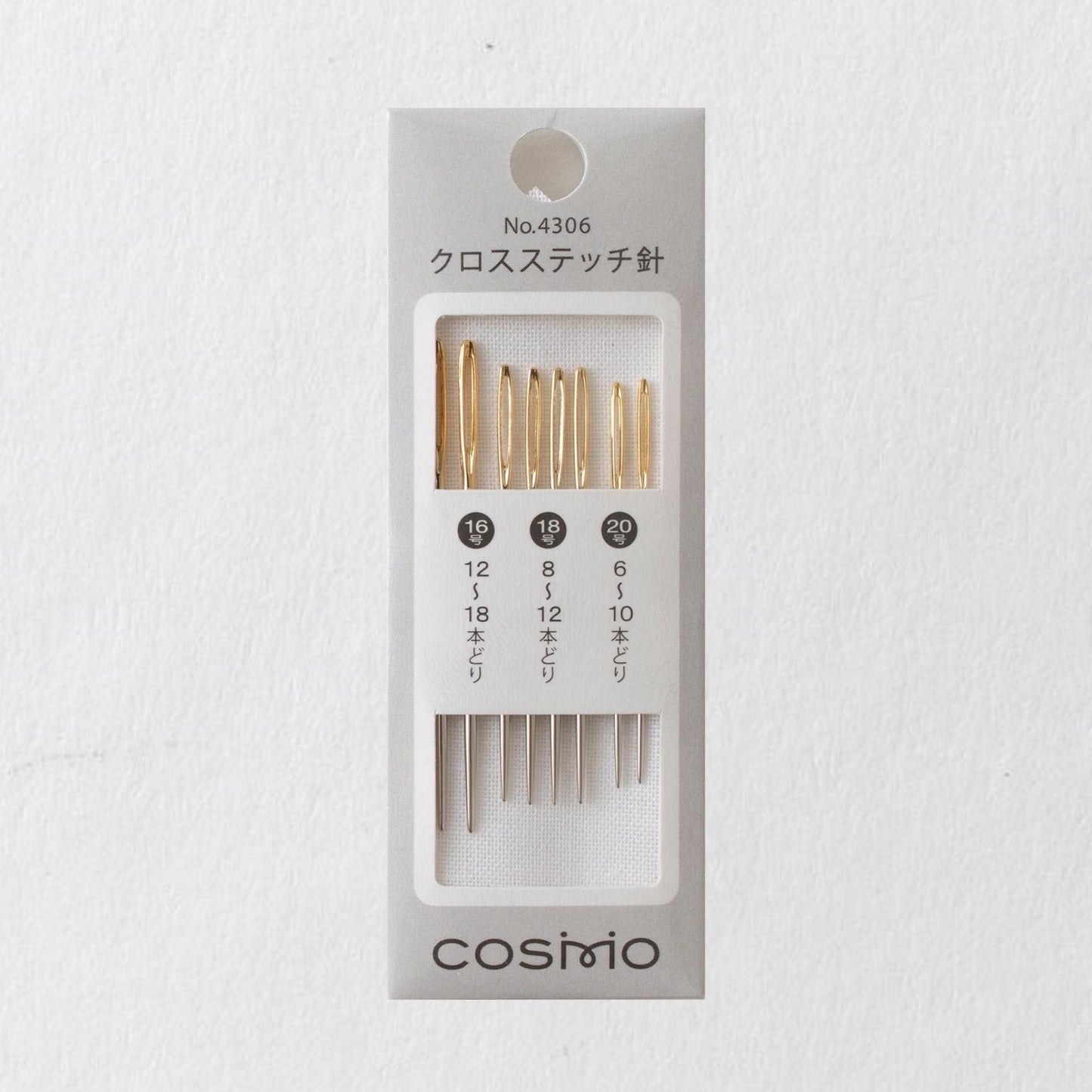 A gray box containing a set of gold-colored knitting needles, with the brand name "COSMO" printed on the box.