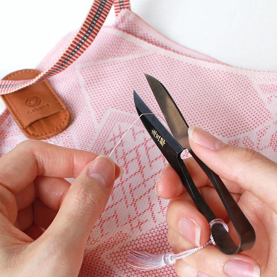 A person's hands are carefully holding a pair of black scissors with a white tassel attached, focused on cutting a string or thread.
