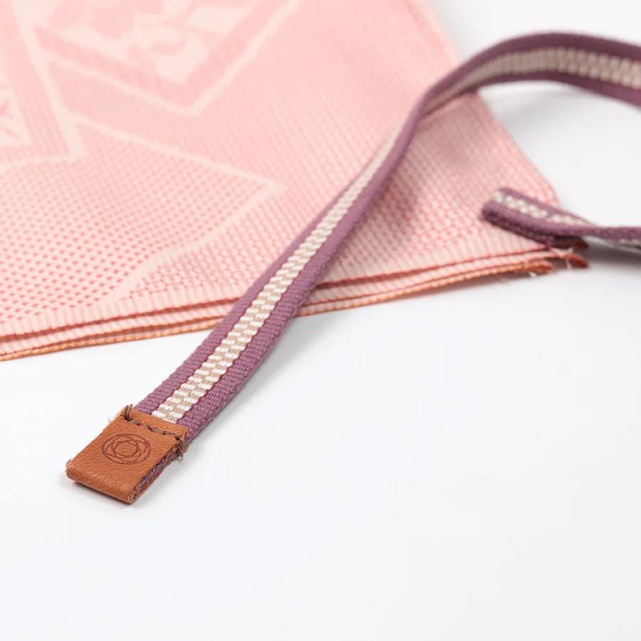 A pink and white patterned fabric item, possibly a cloth or textile, with a brown leather strap or buckle attached to it.