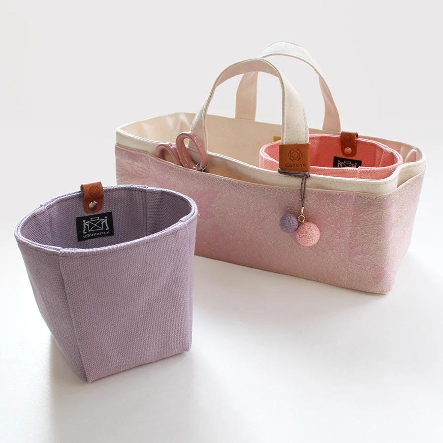 a pink and white tote bag with a purple basket attached to it, sitting on a white surface.
