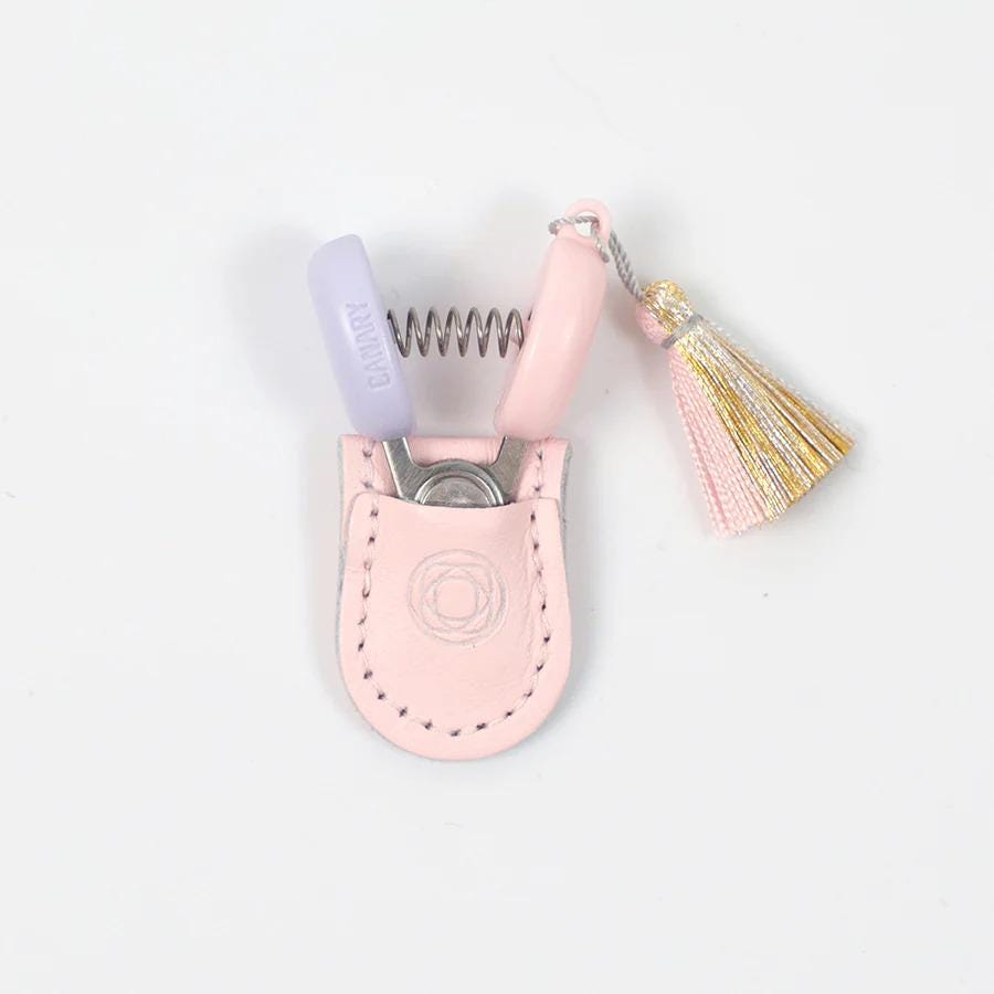 A pair of pink nail clippers with a tassel hanging from the handle, placed in a small pink leather pouch.