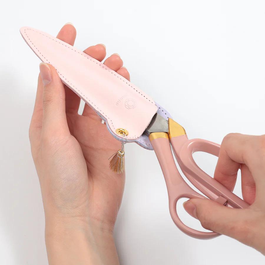 A pair of pink scissors being held by a person's hand.