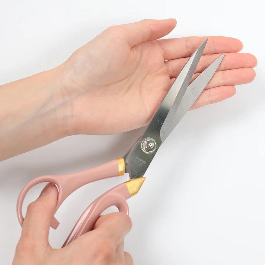 A pair of pink-handled scissors is being held in a person's hand, with the blades open and ready to cut.