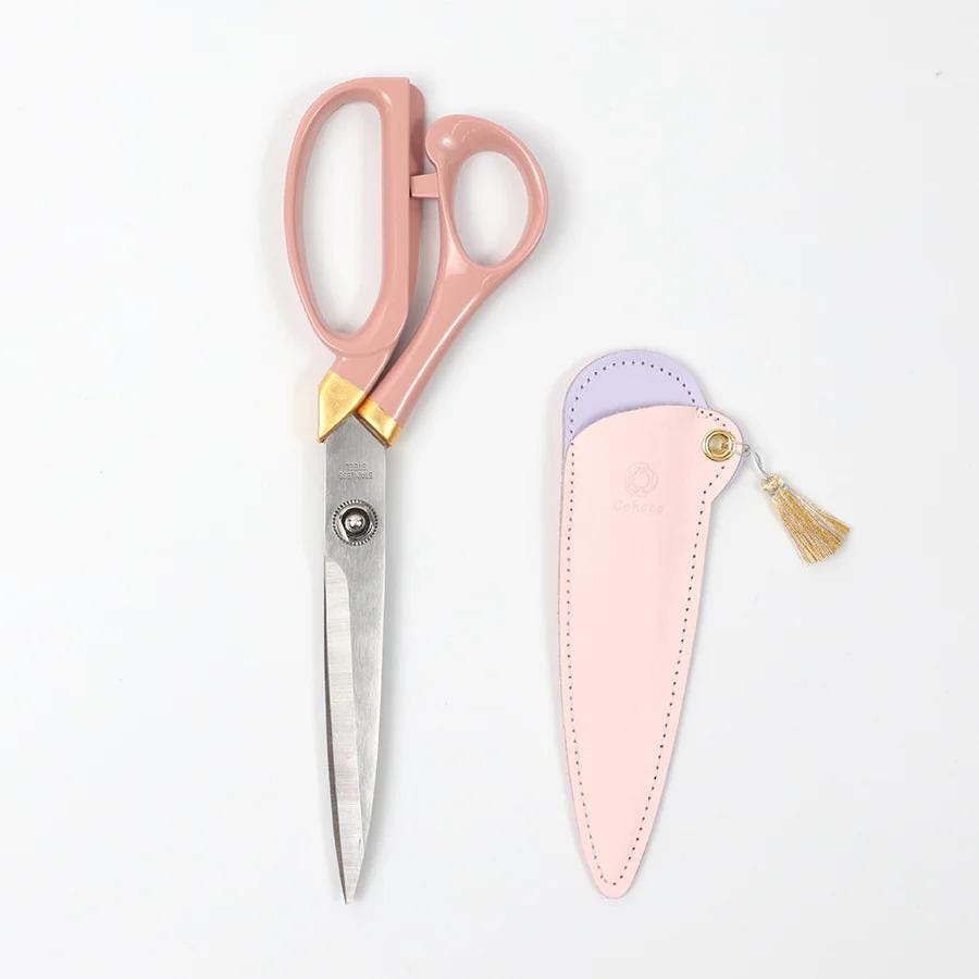 A pair of pink scissors and a pink leather case are shown against a white background.