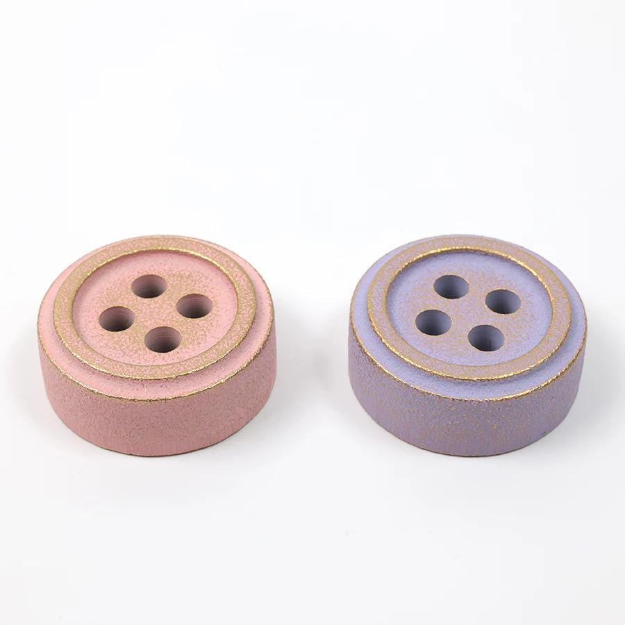 Two ceramic buttons, one pink and one purple, are placed side by side on a white background.