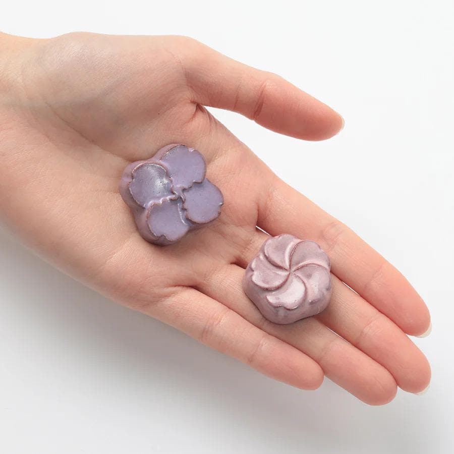 A hand holding two purple flower-shaped objects against a white background.