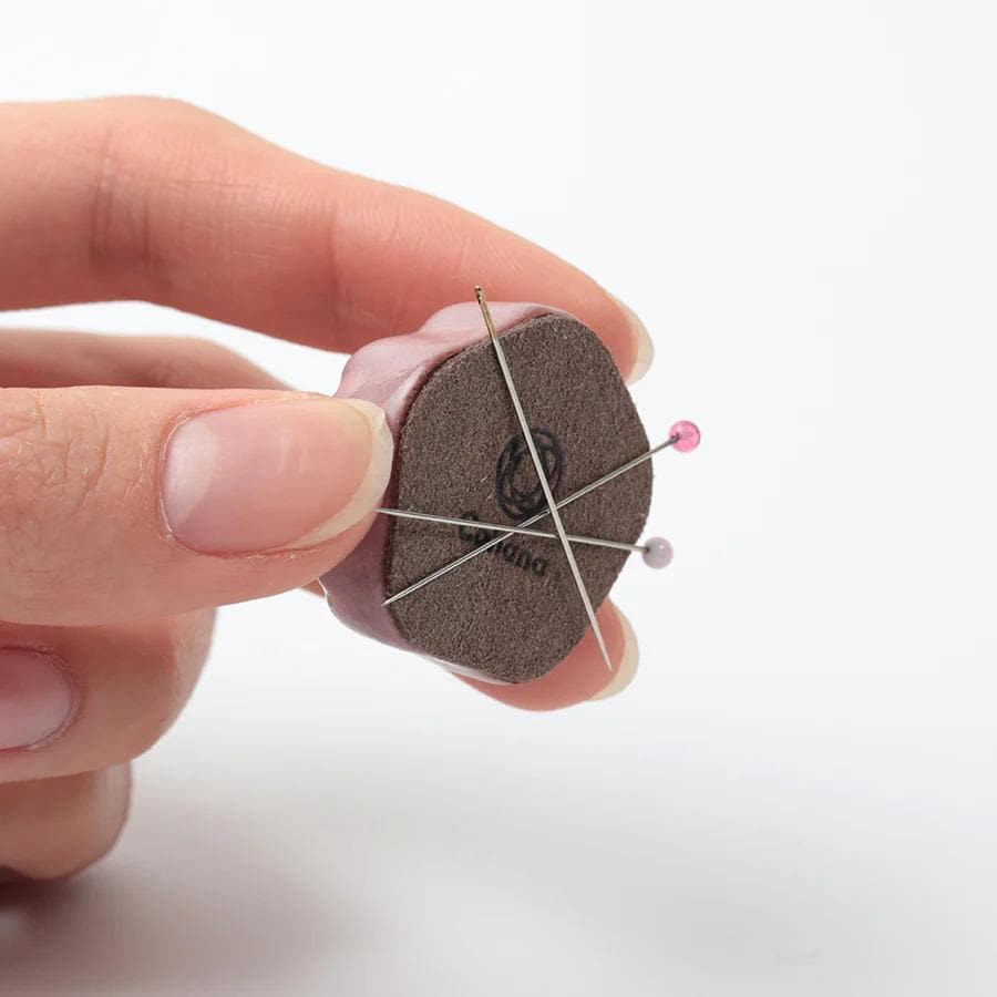 A hand holding a small, round object with a pin hole design on it.