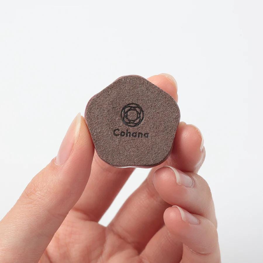 A hand holding a small, brown object with the word "Cohana" printed on it.