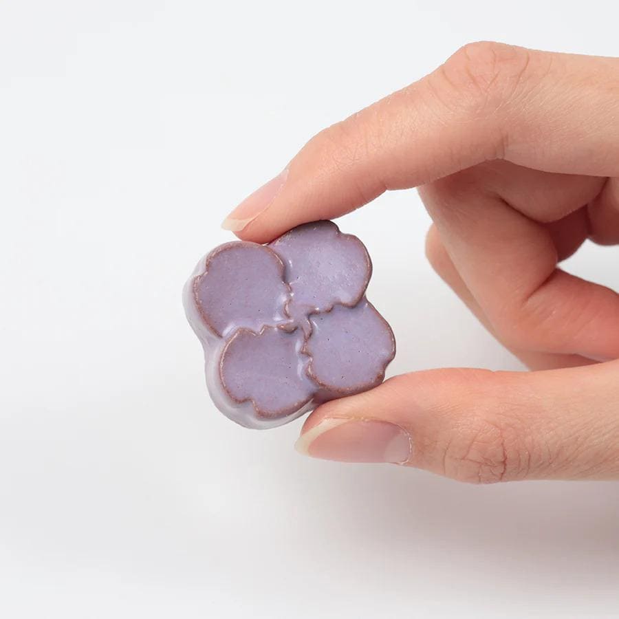 A hand holding a small, purple flower-shaped object.
