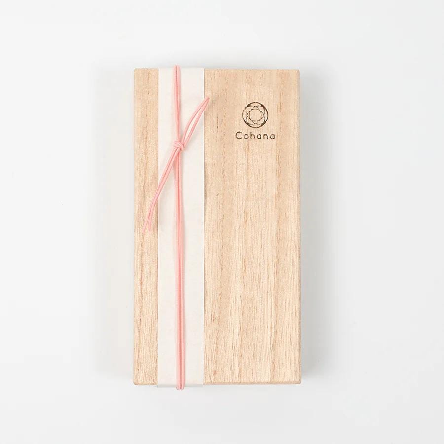 A wooden box with a pink ribbon tied around it, and the word "Cohana" printed on it.