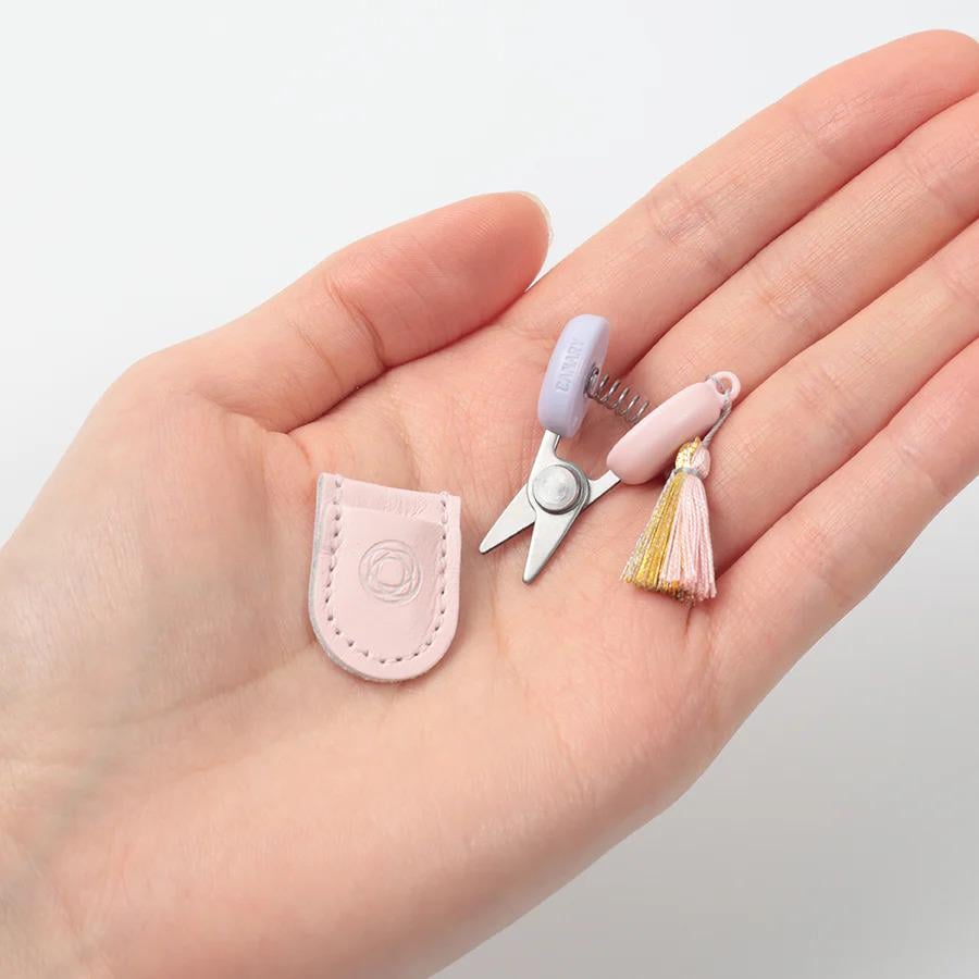 A hand holding a small pair of scissors and a tassel.
