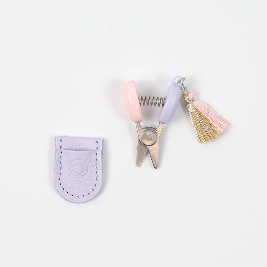 A pair of scissors with a tassel and a small leather pouch are arranged on a white background.