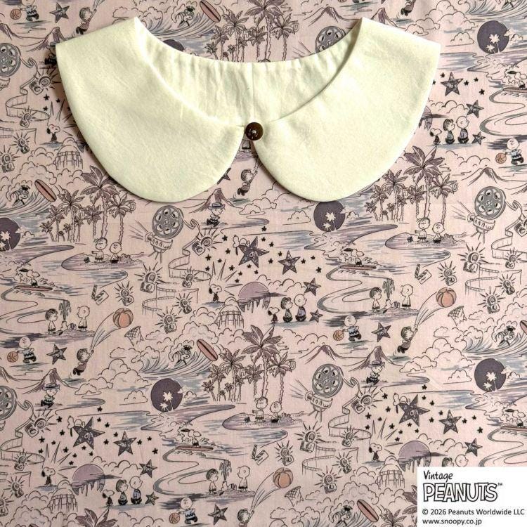 A white collar is placed on a fabric with a whimsical, cartoon-style illustration of various characters and objects, including palm trees, stars, and other whimsical elements.