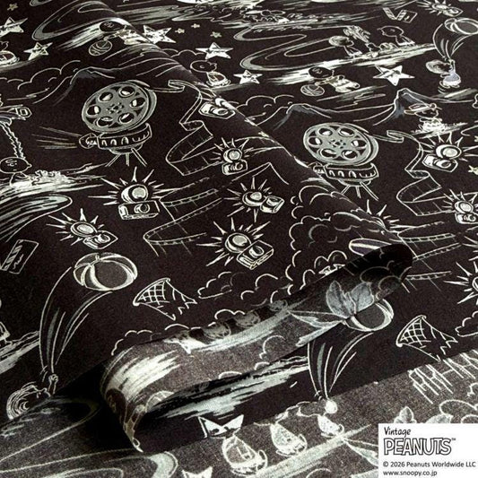 The image is a close-up of a black and white fabric with various illustrations and patterns, including stars, clouds, and other abstract shapes.