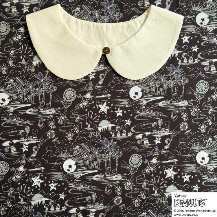 A white collar is displayed against a black and white patterned fabric with various illustrations and designs.
