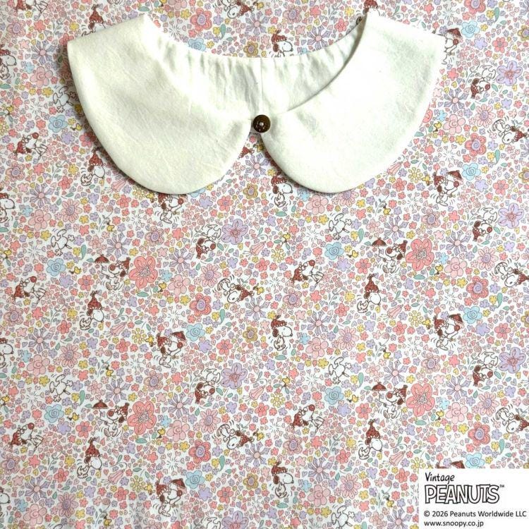 A white collar is placed on a floral fabric with various cartoon characters printed on it.