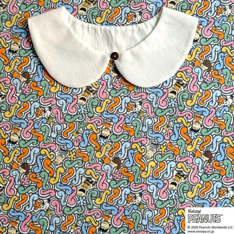 A white collar is placed on a colorful fabric with a repeating pattern of cartoon characters.