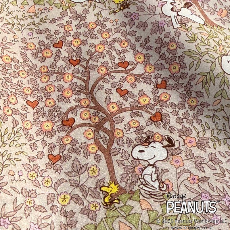 A vintage Peanuts-themed fabric with a tree adorned with flowers and hearts, along with Snoopy and Woodstock sitting under the tree.
