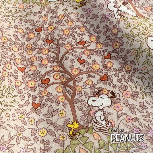 A vintage Peanuts-themed fabric with a tree adorned with flowers and hearts, along with Snoopy and Woodstock sitting under the tree.