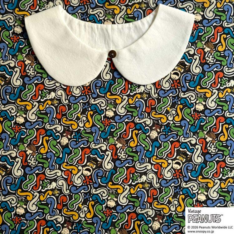 A white collar is placed on a colorful, abstract fabric with various shapes and patterns.