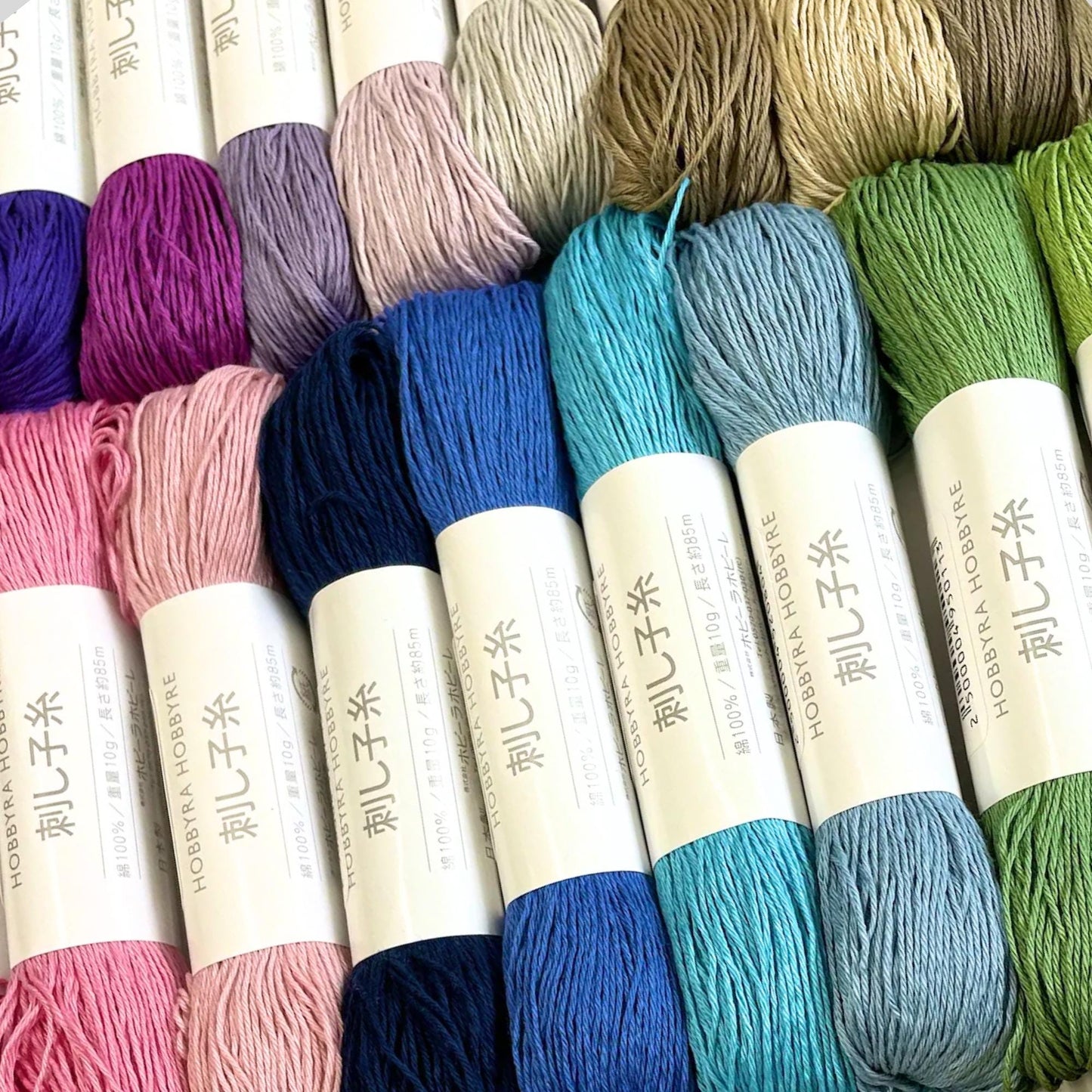 A collection of colorful yarn skeins in various shades, including pink, blue, green, and other pastel hues, arranged in rows.