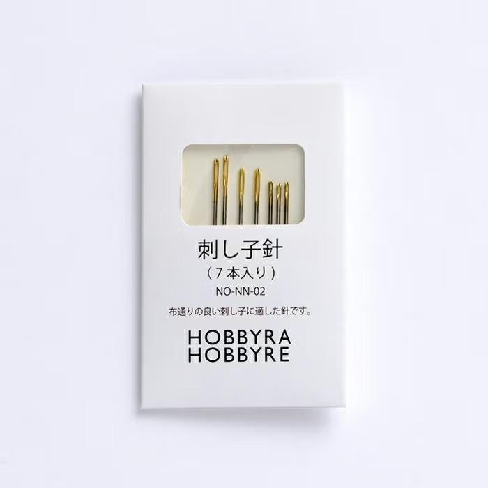 A white box containing a set of gold-colored sewing needles, with the text "HOBBY RE" printed on it.