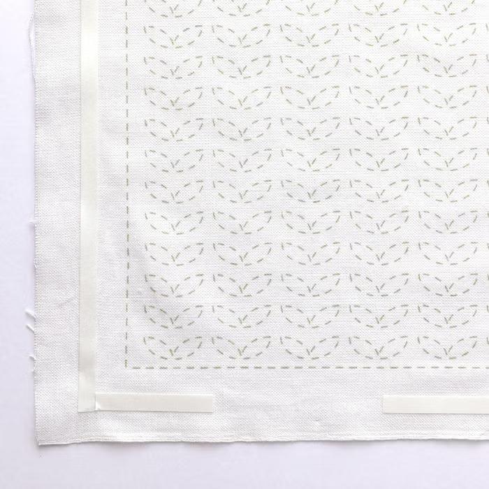 a close-up view of a white fabric with a repeating pattern of green leaves or flowers. The pattern is visible on the fabric, creating a visually appealing design.