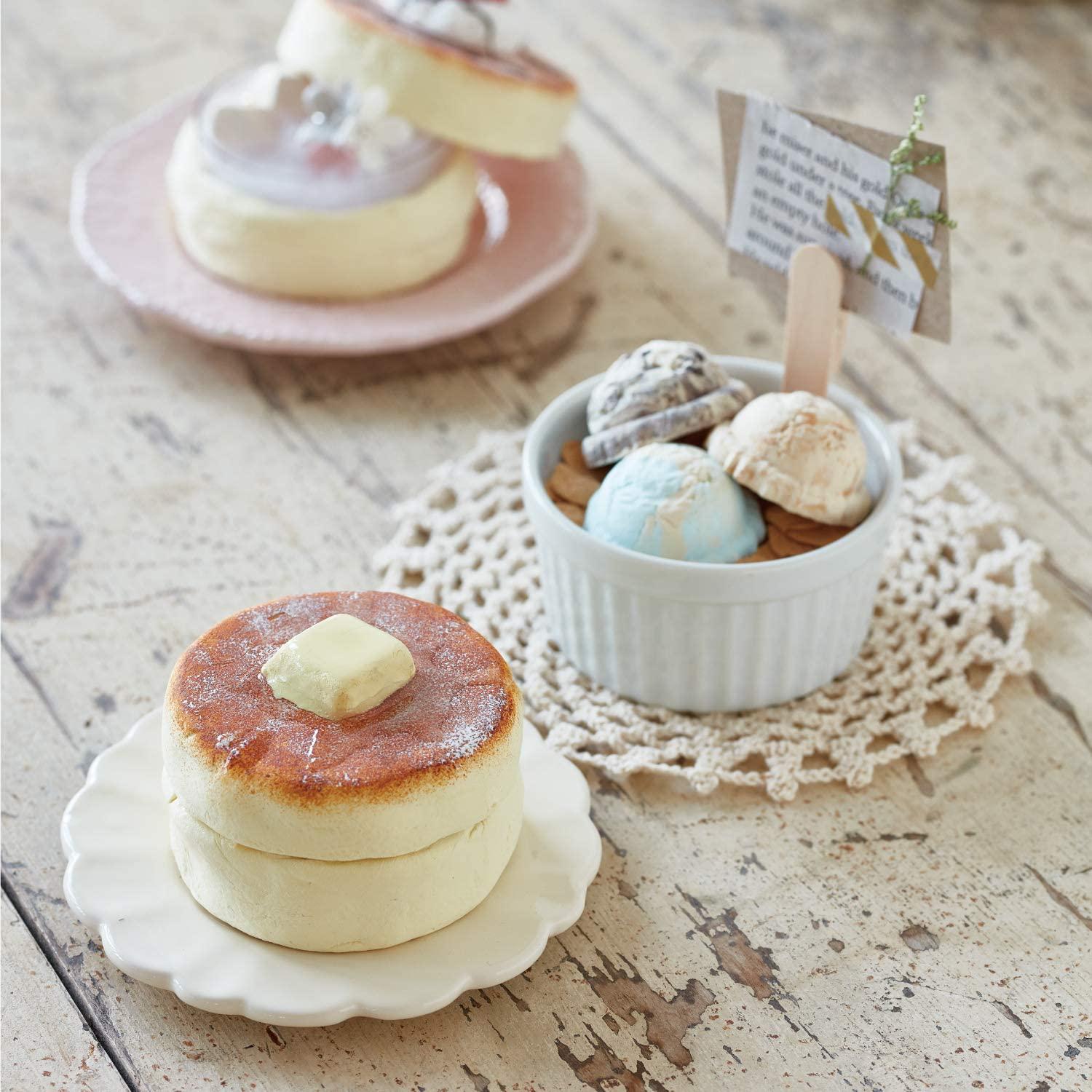 a variety of desserts, including a stack of pancakes with butter, a bowl of ice cream, and a plate of pastries. The desserts are arranged on a wooden table, creating an inviting and visually appealing display.