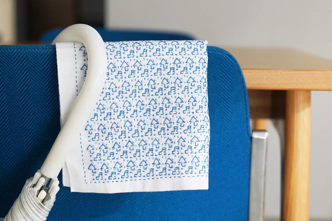 A white umbrella with blue patterns is hanging on a blue chair.