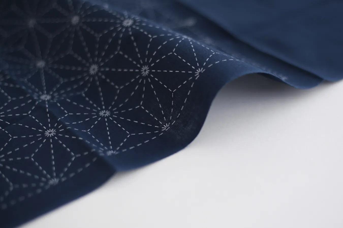 a close-up view of a dark blue fabric with a geometric pattern of white lines and dots, creating a visually striking contrast against the white background.