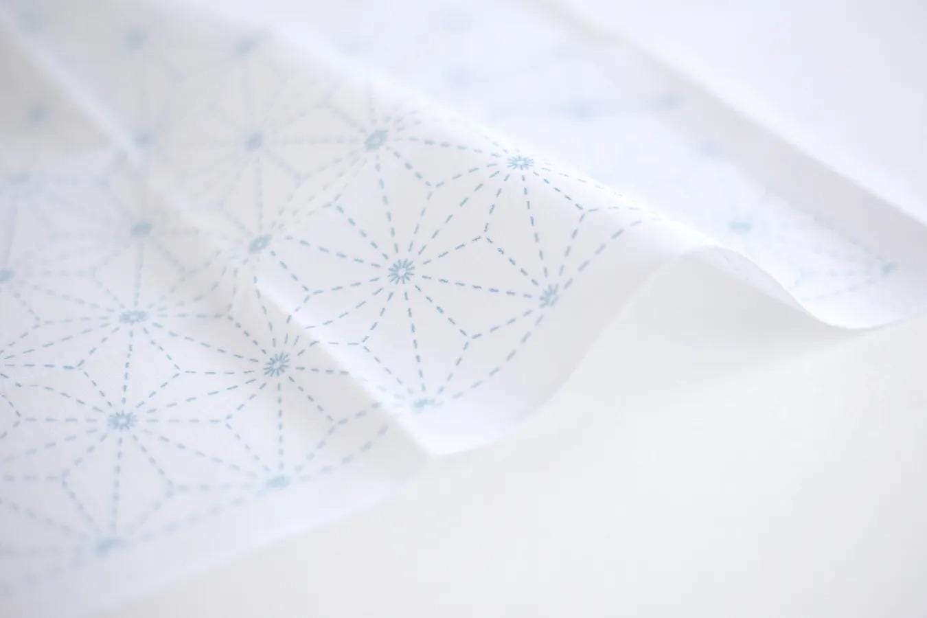 a close-up view of a white fabric with a blue geometric pattern, featuring a repeating star-like design.
