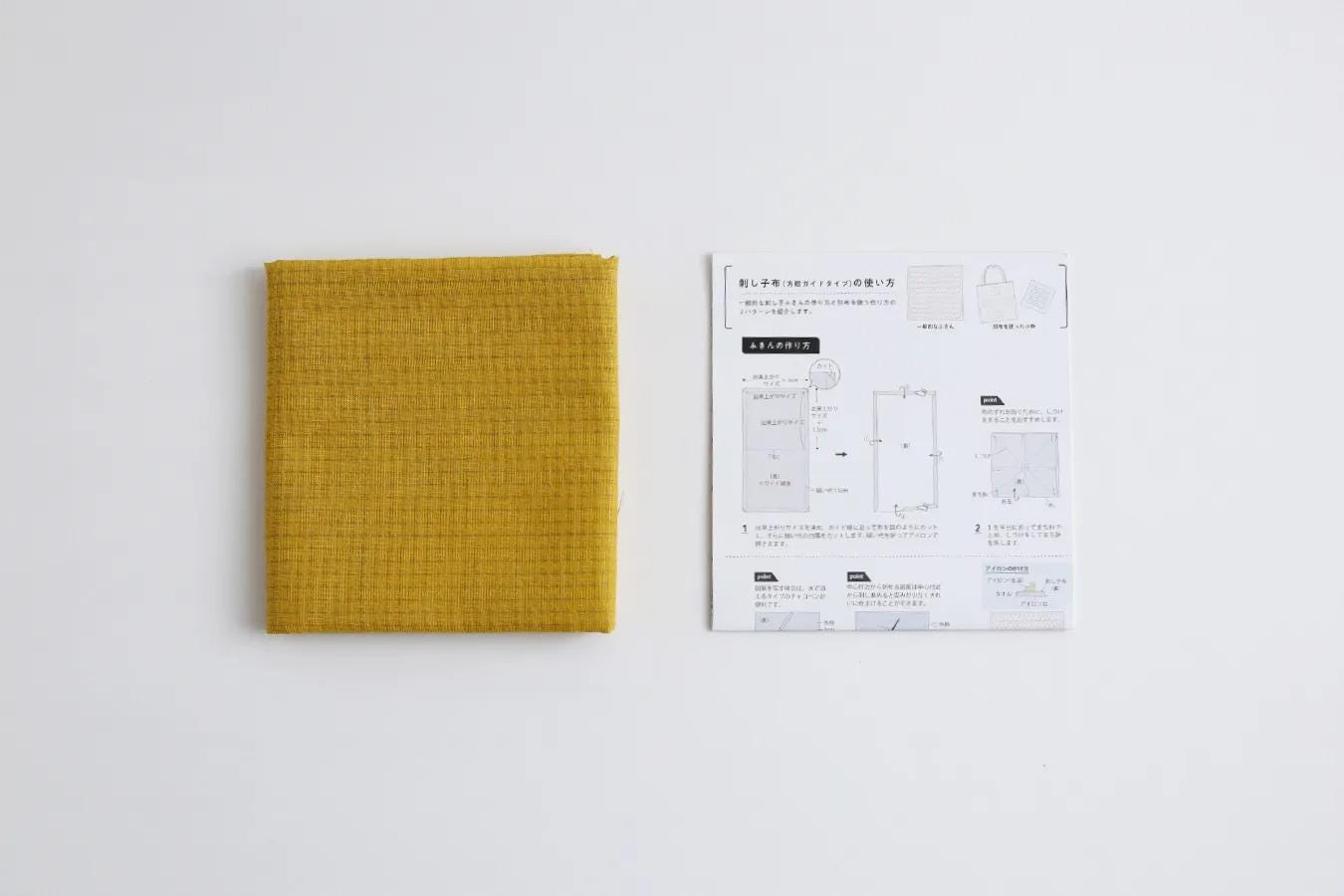 a yellow fabric and a printed instruction manual for a product, likely a bag or a piece of clothing, placed on a white background.