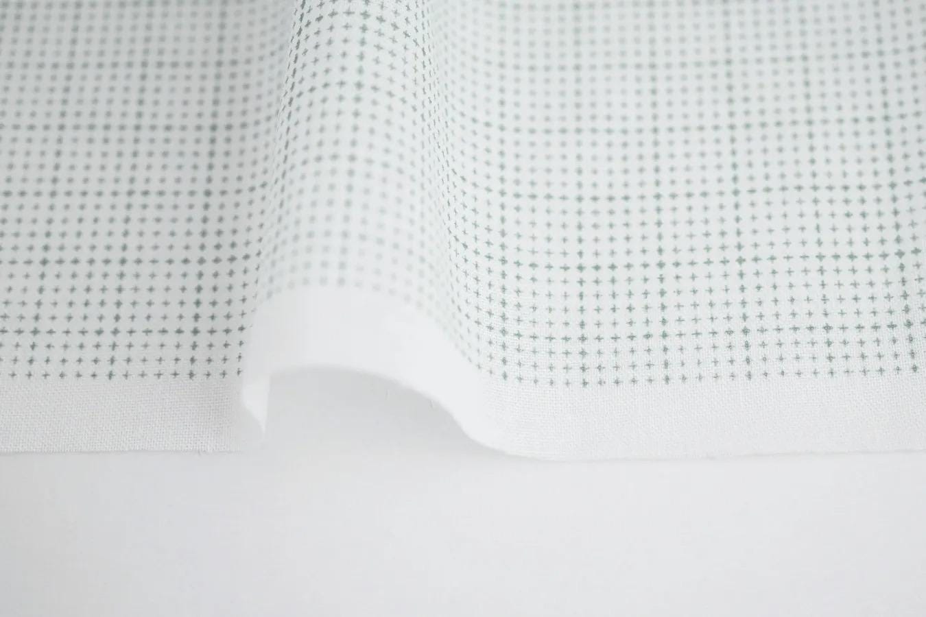 a close-up view of a white fabric with a grid pattern of small green dots or circles.
