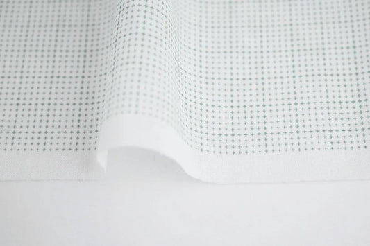 a close-up view of a white fabric with a grid pattern of small green dots or circles.