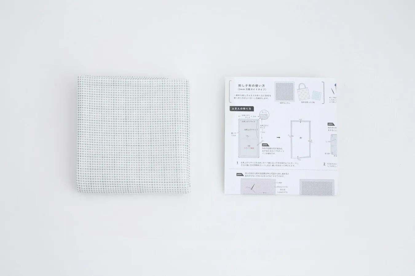 a square piece of fabric with a dotted pattern and a printed diagram with text and illustrations, both placed on a white background.