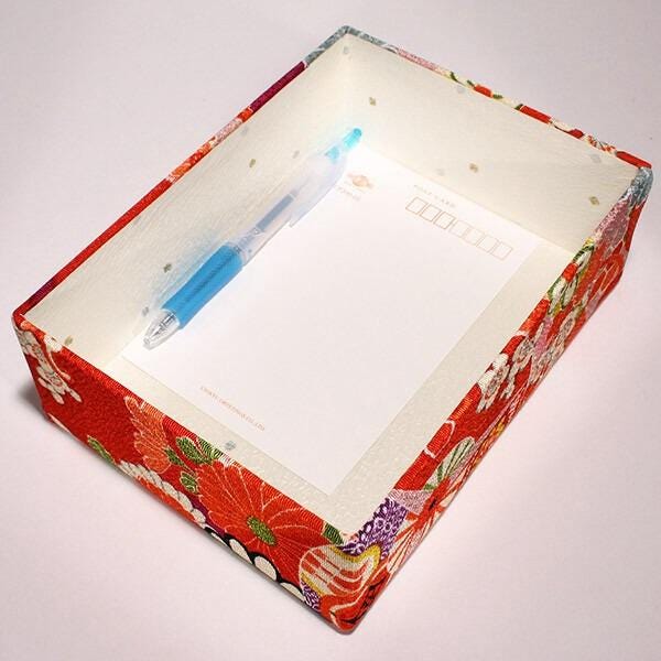 A red and white floral box with a blue pen inside, placed on a white surface.