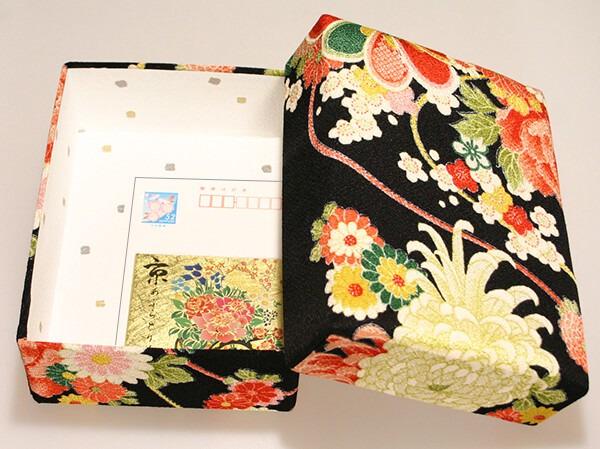 an open box with a floral pattern on the lid and a white envelope inside.