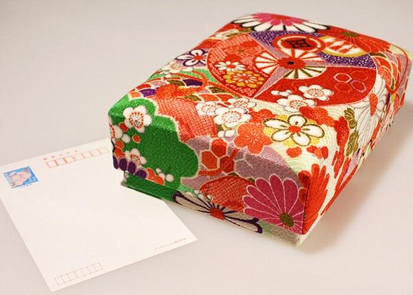 A colorful, patterned box with a floral design sits on a white surface next to a blank white card.