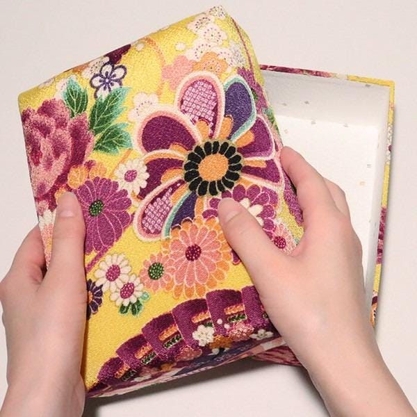 A pair of hands holding a colorful, floral-patterned box with a yellow and pink design.