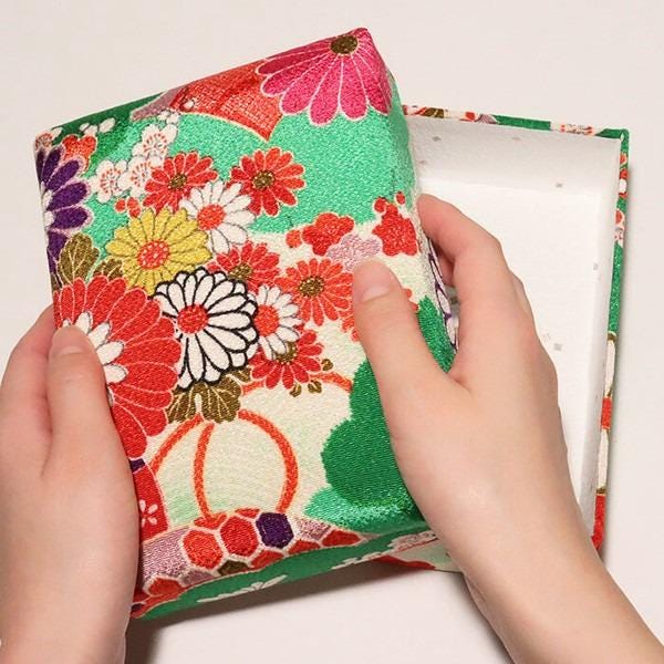 A pair of hands holding a colorful, patterned box with a floral design.