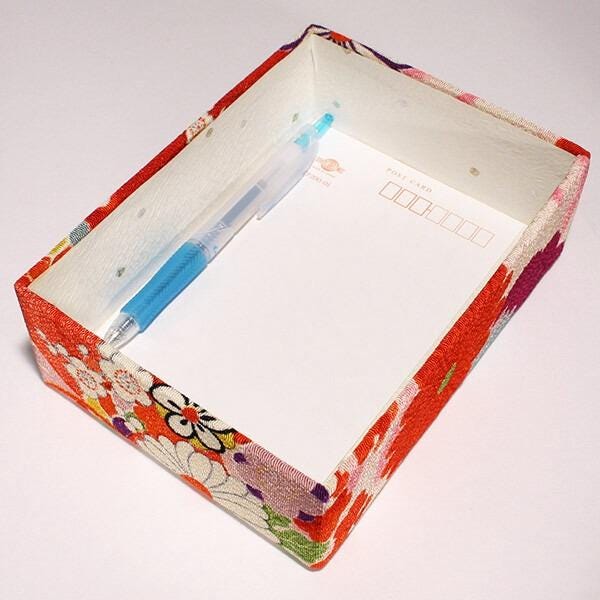A red and white floral box with a blank white paper inside, along with a blue pen.