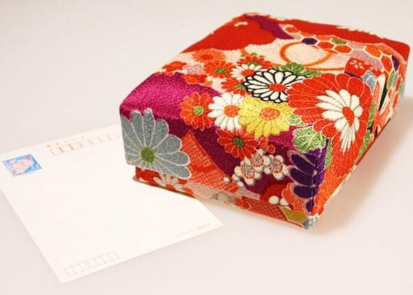 A colorful, patterned box with a floral design sits on a white surface next to a blank white card.