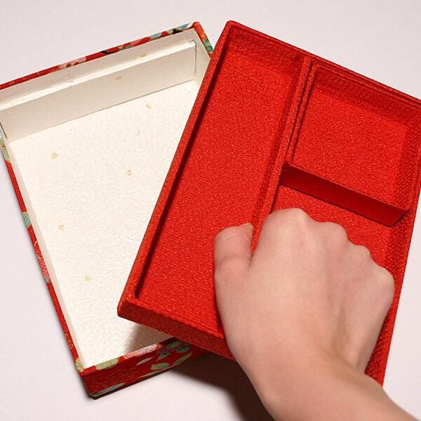A hand is holding a red box with a white interior, which appears to be an empty box.