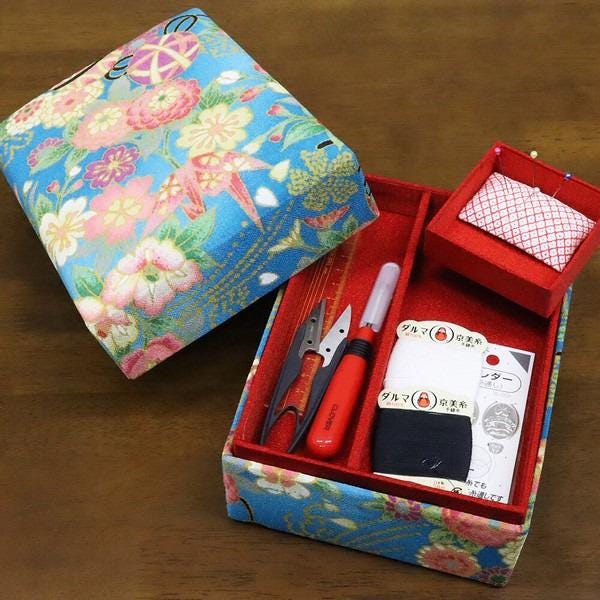 A colorful box with a floral pattern, containing sewing tools and materials, including scissors, pins, and a red box with a white pattern.
