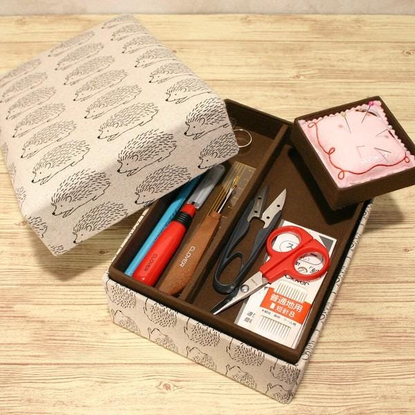 A wooden box with a lid and a small box with a lid are shown, along with various sewing and crafting tools such as scissors, a needle, and a pin cushion.
