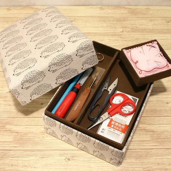 A sewing kit containing various tools and materials, including scissors, needles, pins, and a pattern, is displayed on a wooden surface.