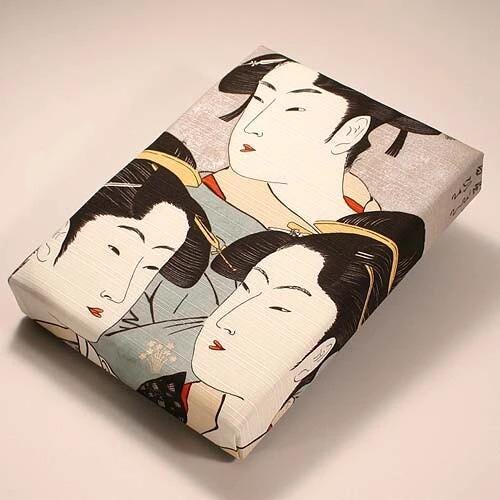 a rectangular gift box with a printed design of three stylized female faces on the front.